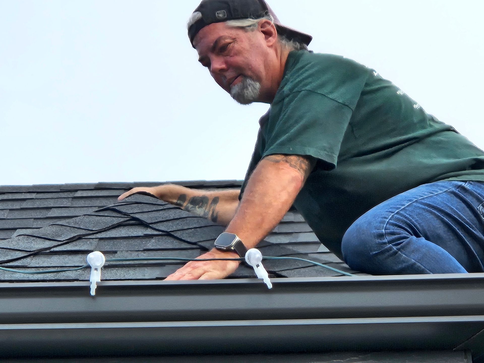 Man on a roof installing Christmas lights, using clips along the gutter.