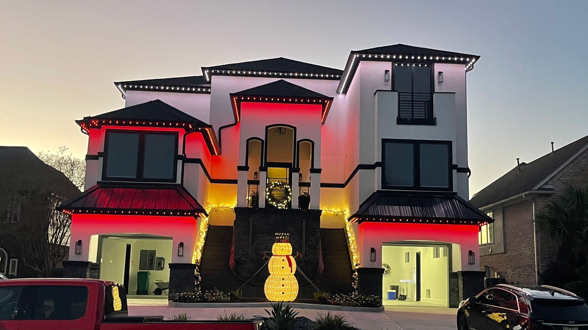 House decorated with red and white Christmas lights, snowman decoration in front.