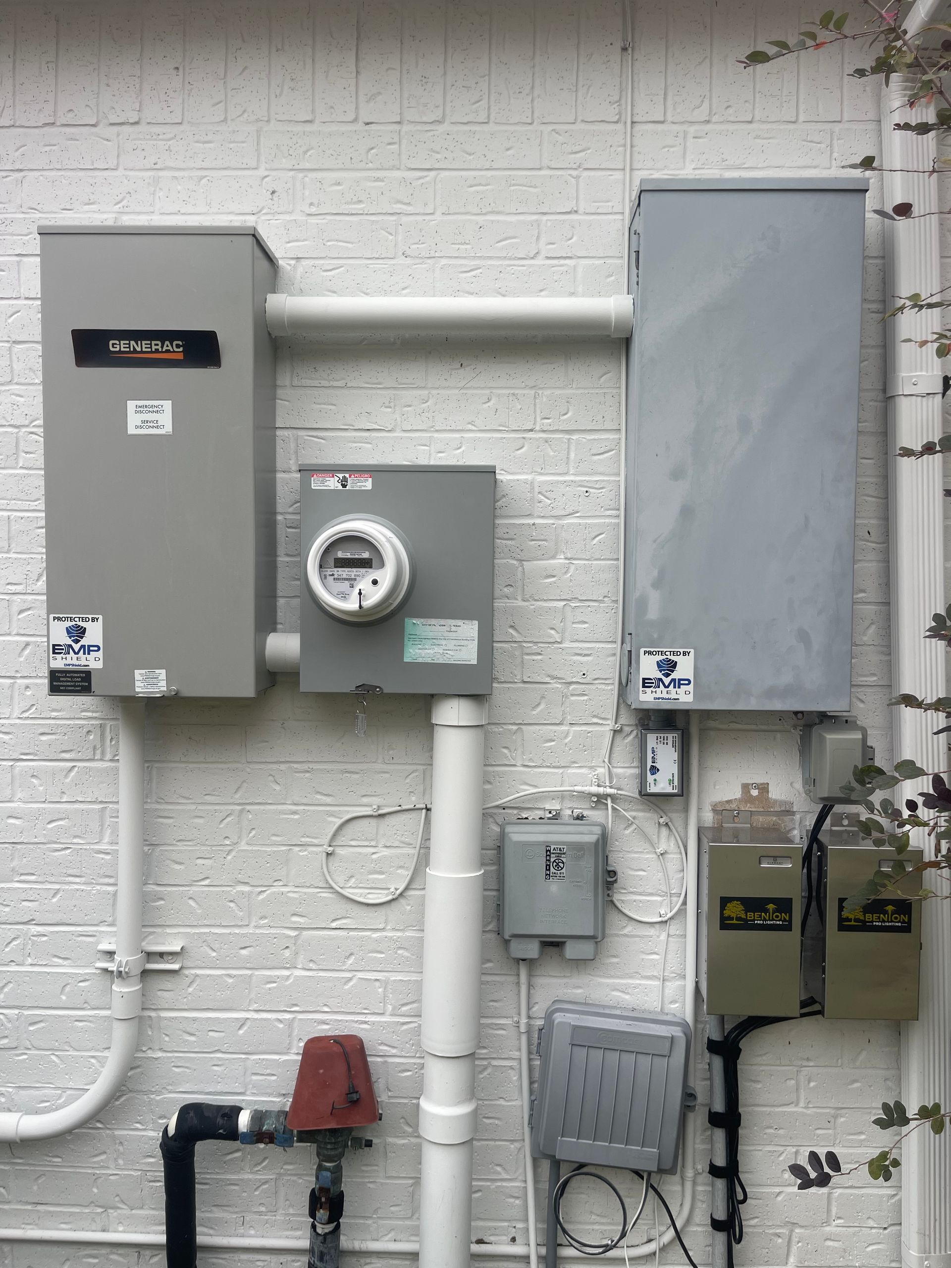 Electrical equipment mounted on a white brick wall, including boxes, conduit, a meter, and pipes.