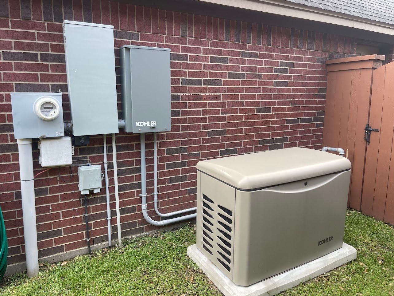 Generator and electrical boxes on a brick wall, next to a brown wooden gate.