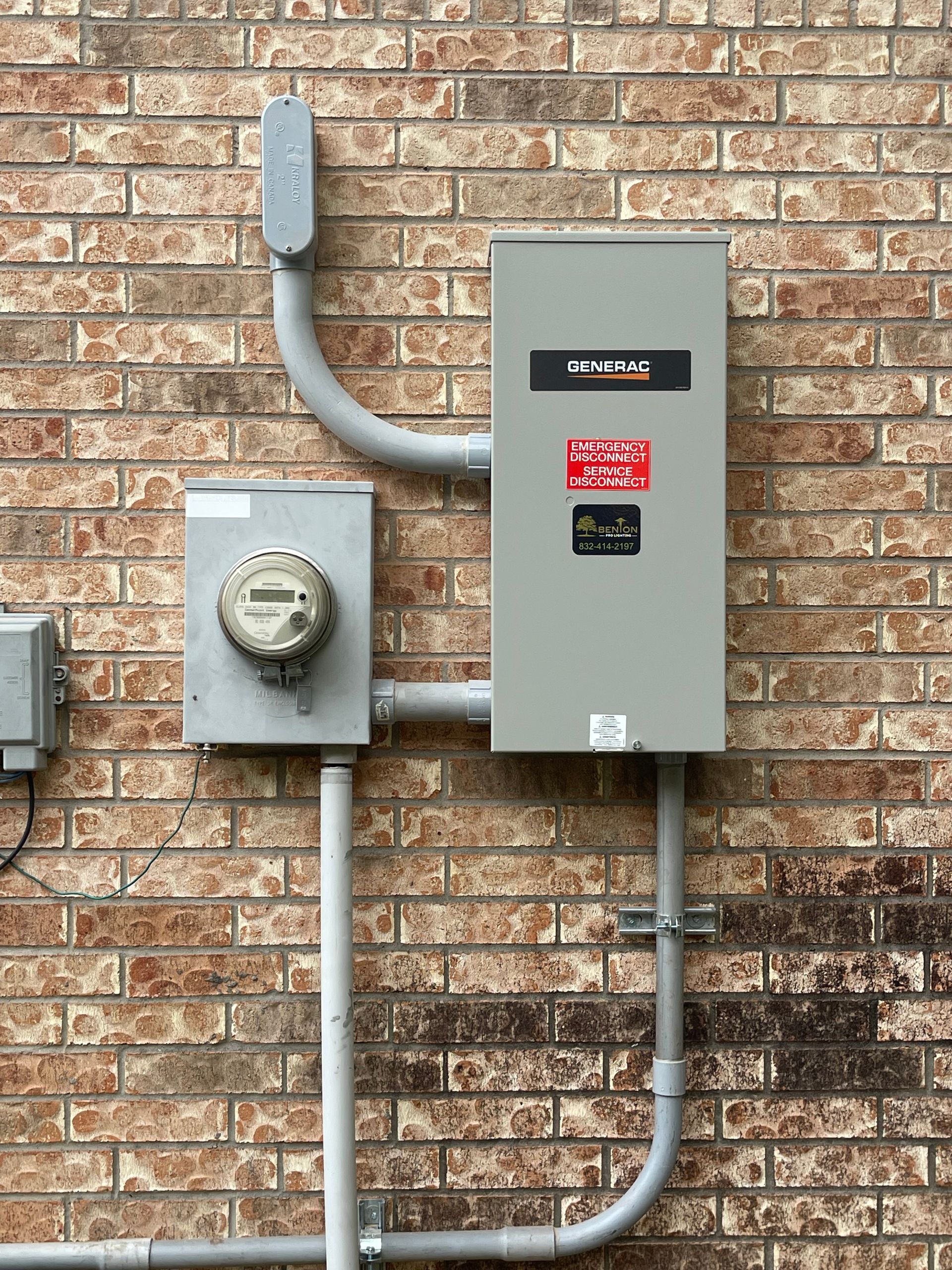 Gray electrical panel and meter box on a brick wall. Conduit connects them to each other and an upper device.
