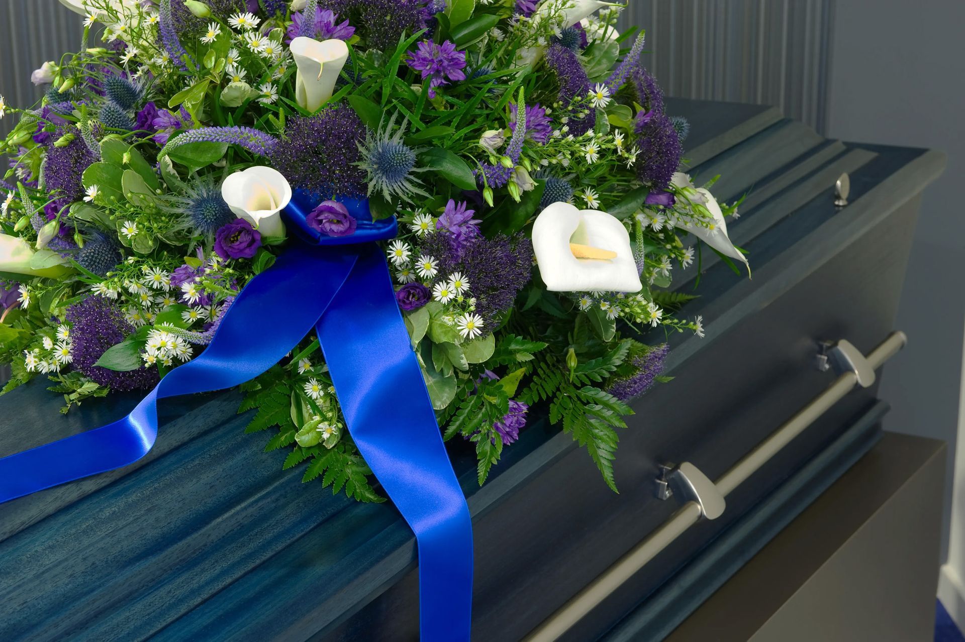Blue casket adorned with purple and white floral arrangement and blue ribbon.