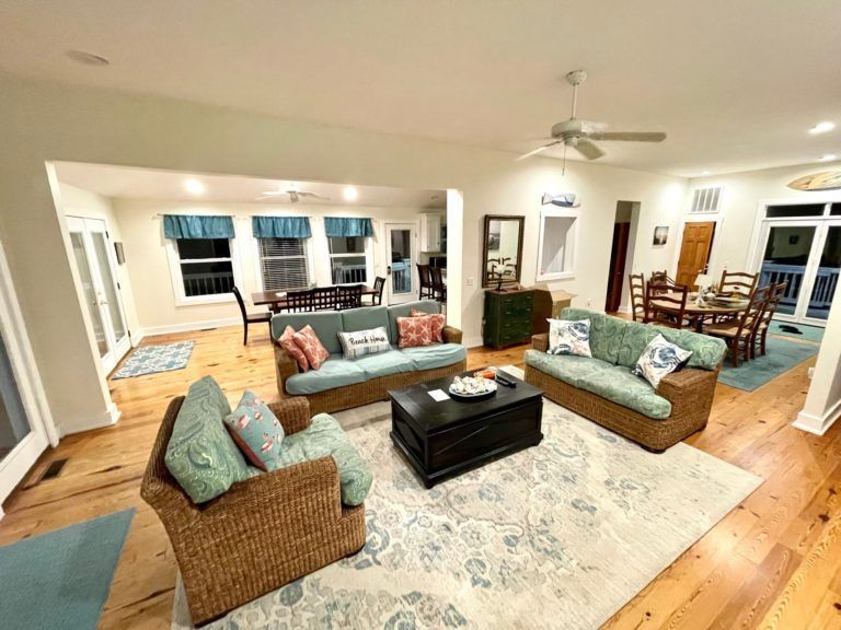Spacious living room with wicker furniture, area rug, and open to dining area.