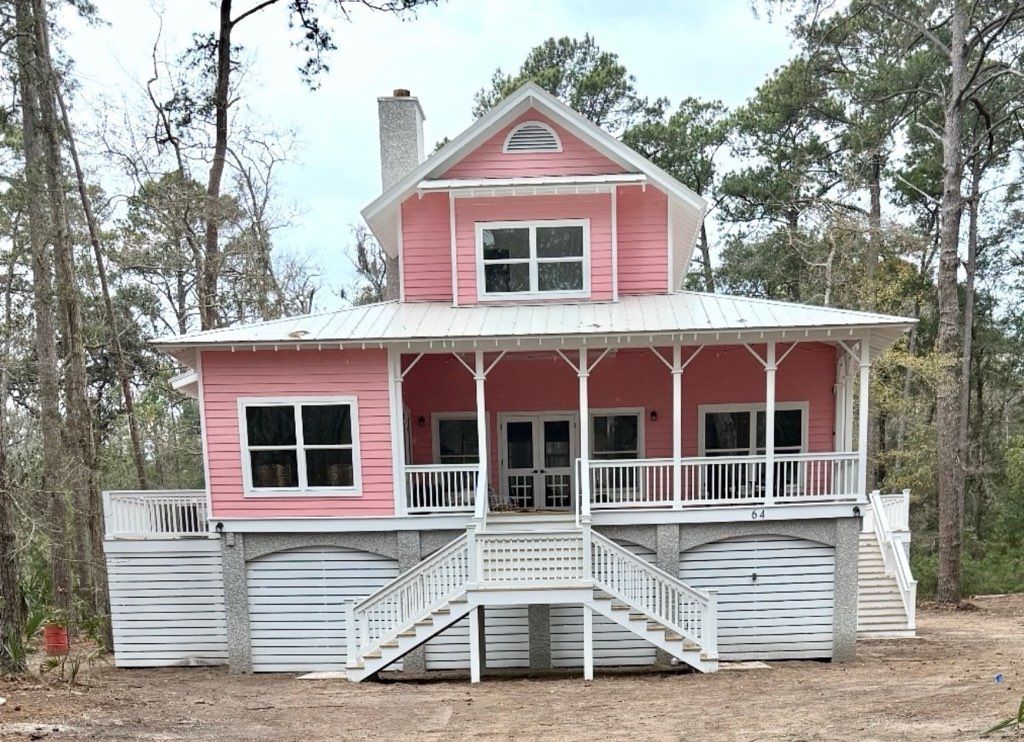 Purple beach house on stilts with porch and wooden stairs leading to the entrance, blue sky background.