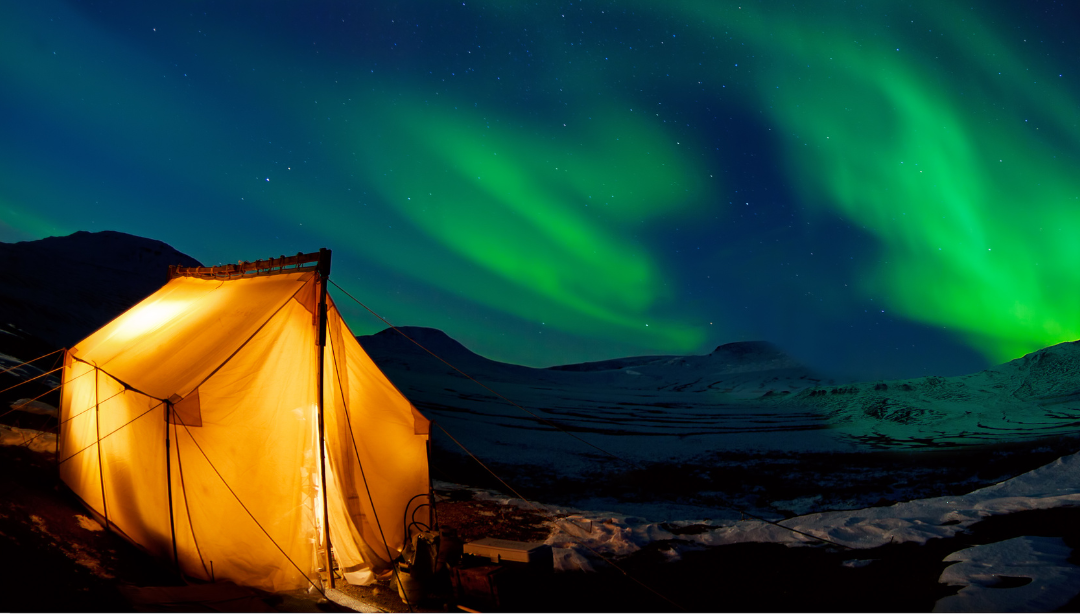 A tent is lit up in front of the aurora borealis.