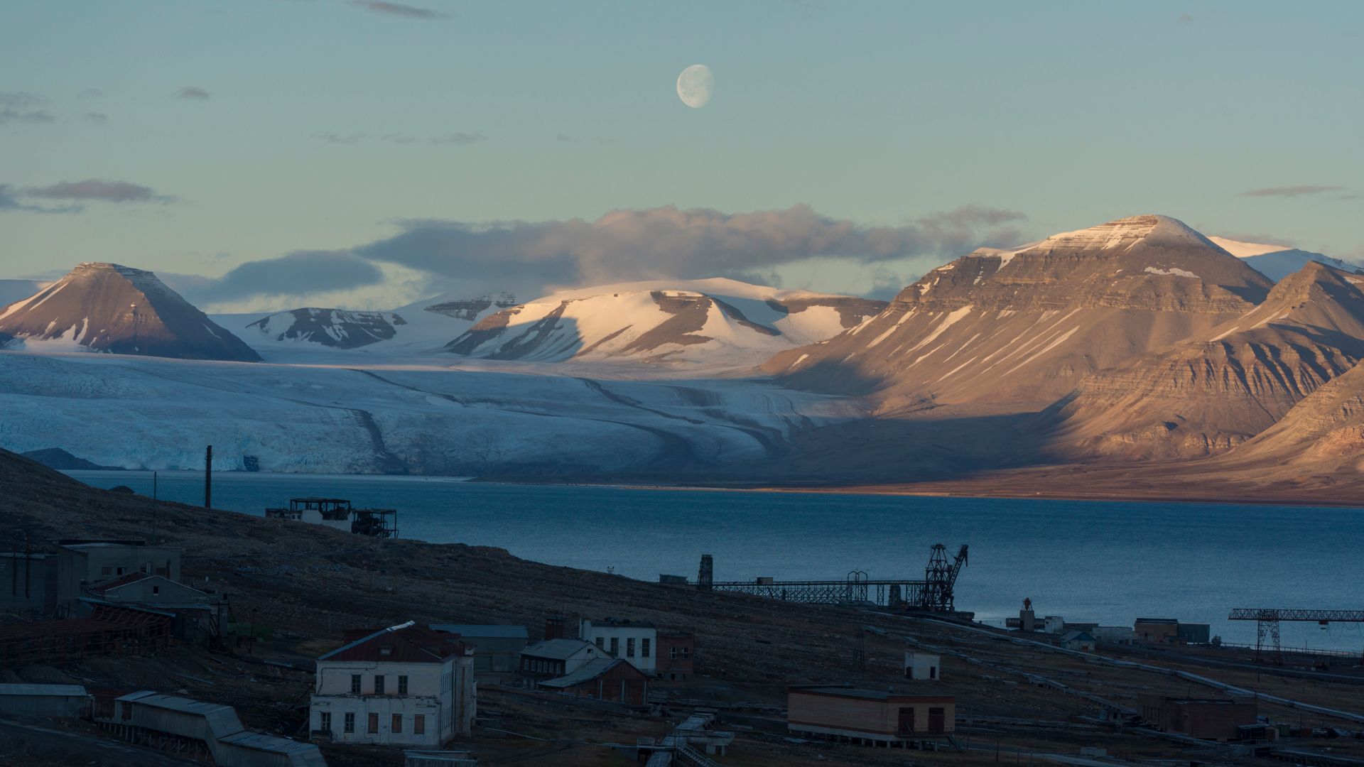 A view of a lake with mountains in the background and a full moon in the sky.