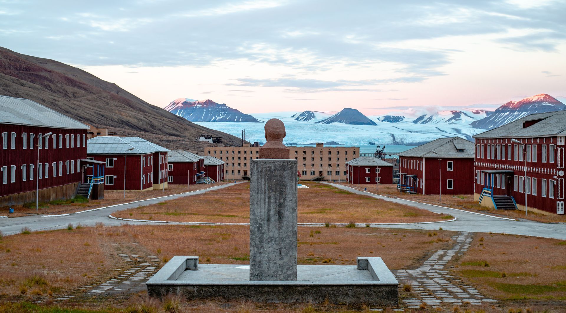 A statue in the middle of a row of buildings with mountains in the background.