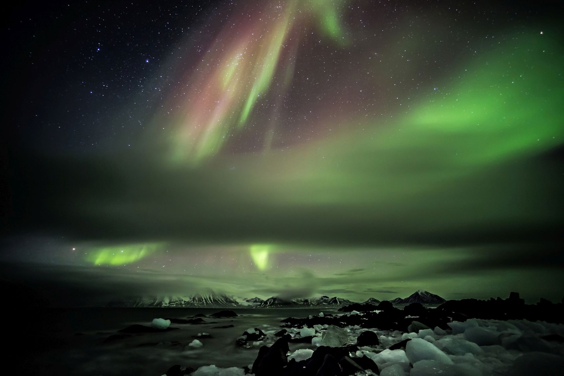 The aurora borealis is glowing in the night sky over a body of water.