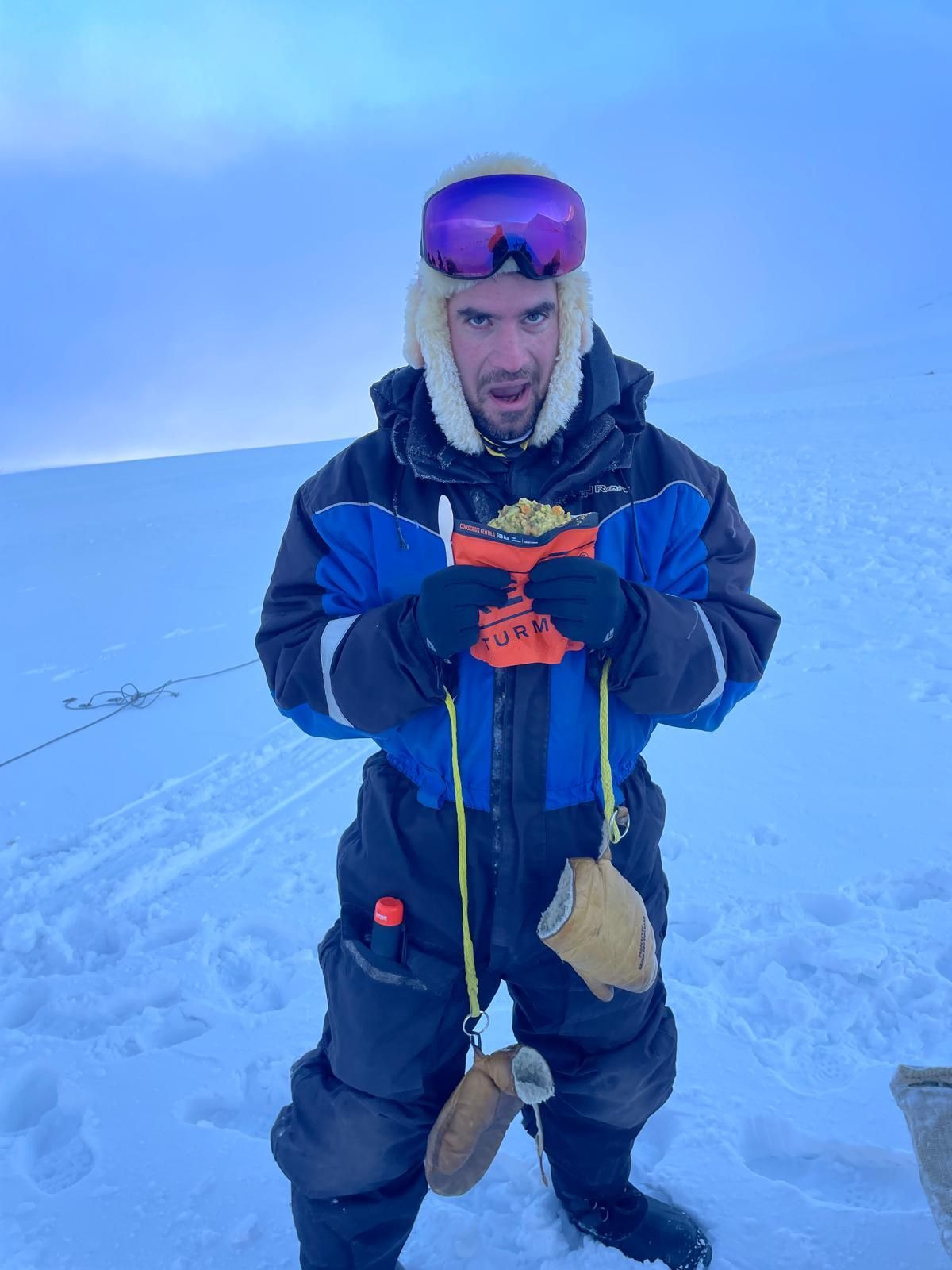A man in a ski suit is standing in the snow holding a book.