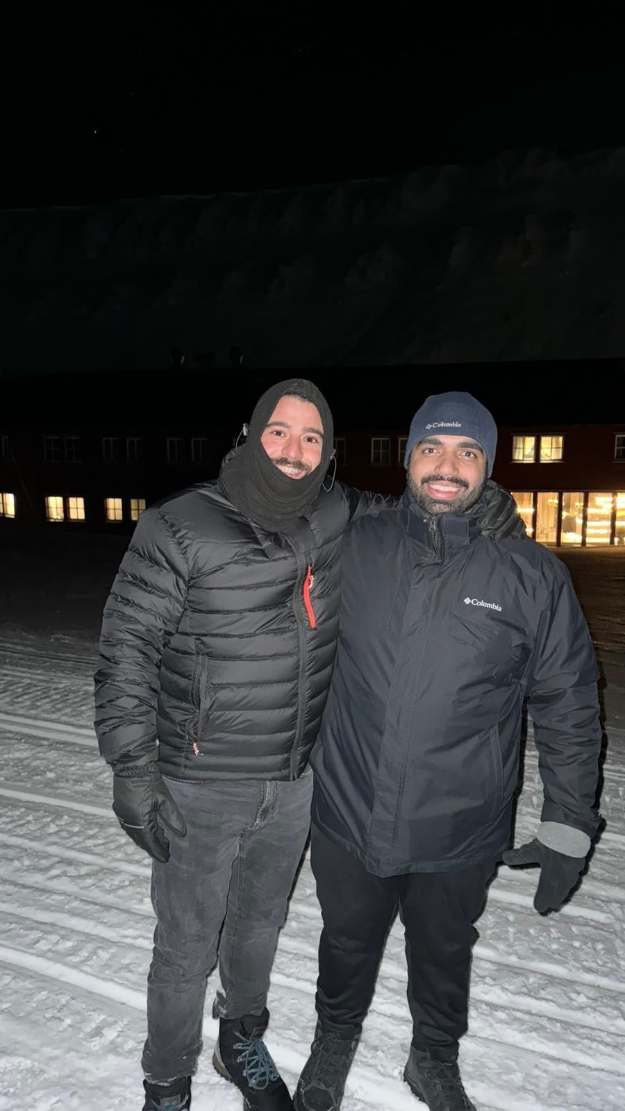 Two men are standing next to each other in the snow at night.