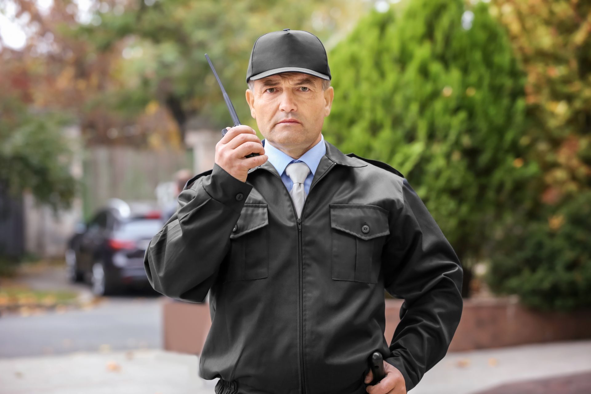 A security guard patrol officer in a black uniform uses a walkie-talkie while monitoring.