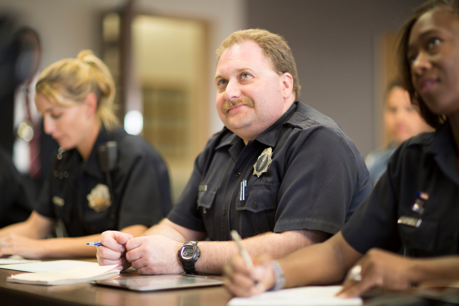 Uniformed officers seated at a table taking notes during a law enforcement training session.