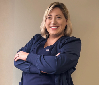 Woman with blonde hair smiles next to a light-colored horse in a barn.