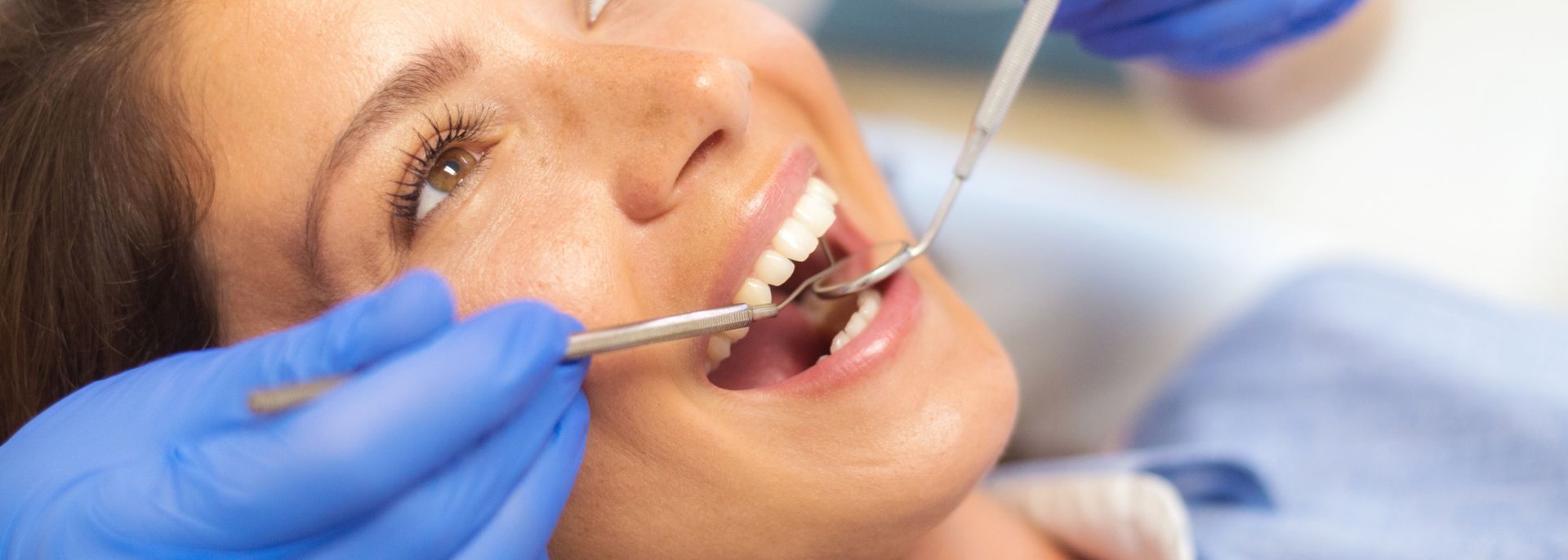 Dentist examining woman's teeth with dental mirror during routine checkup.