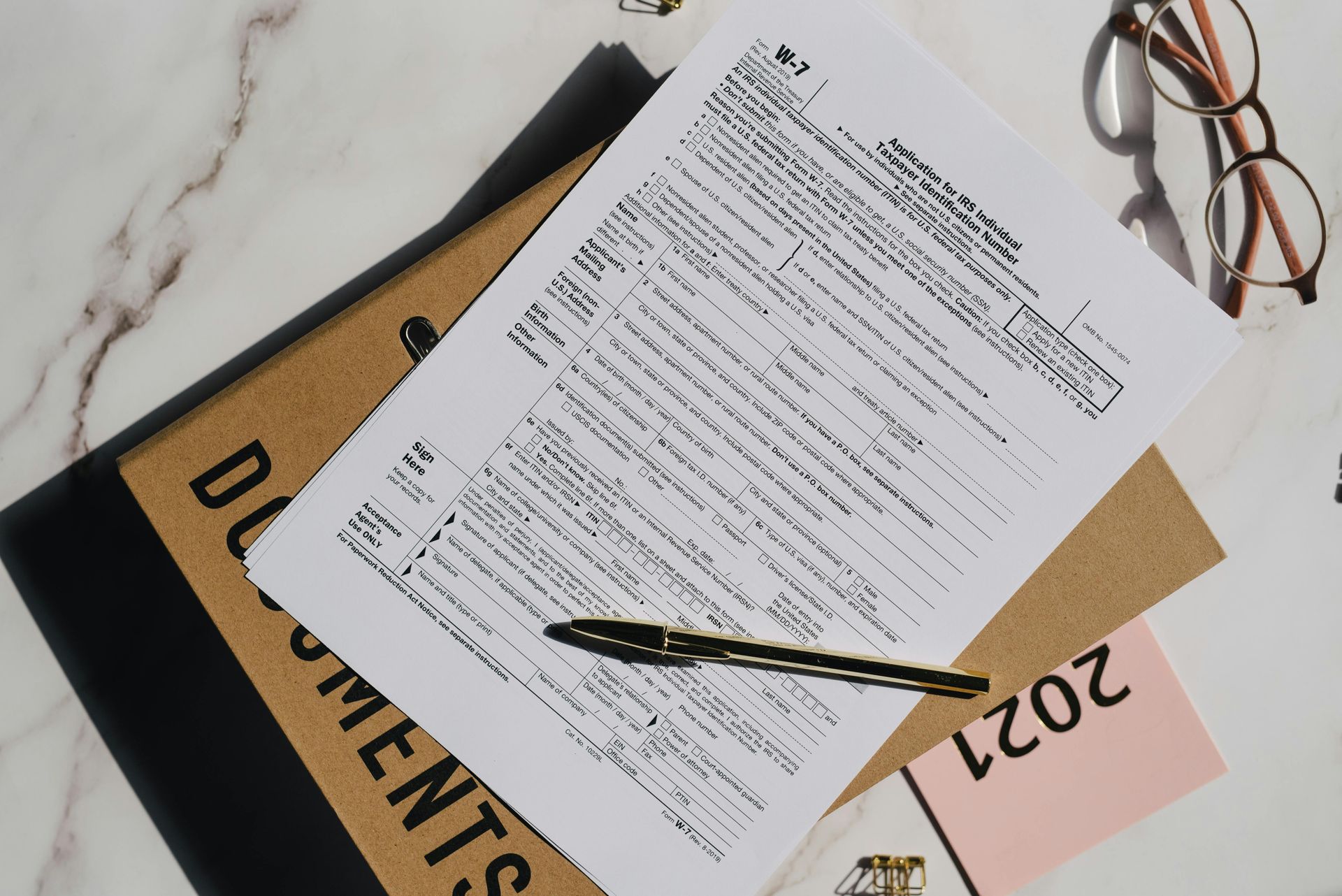 Documents, pen, and glasses on a desk; a tax form is on top of a 