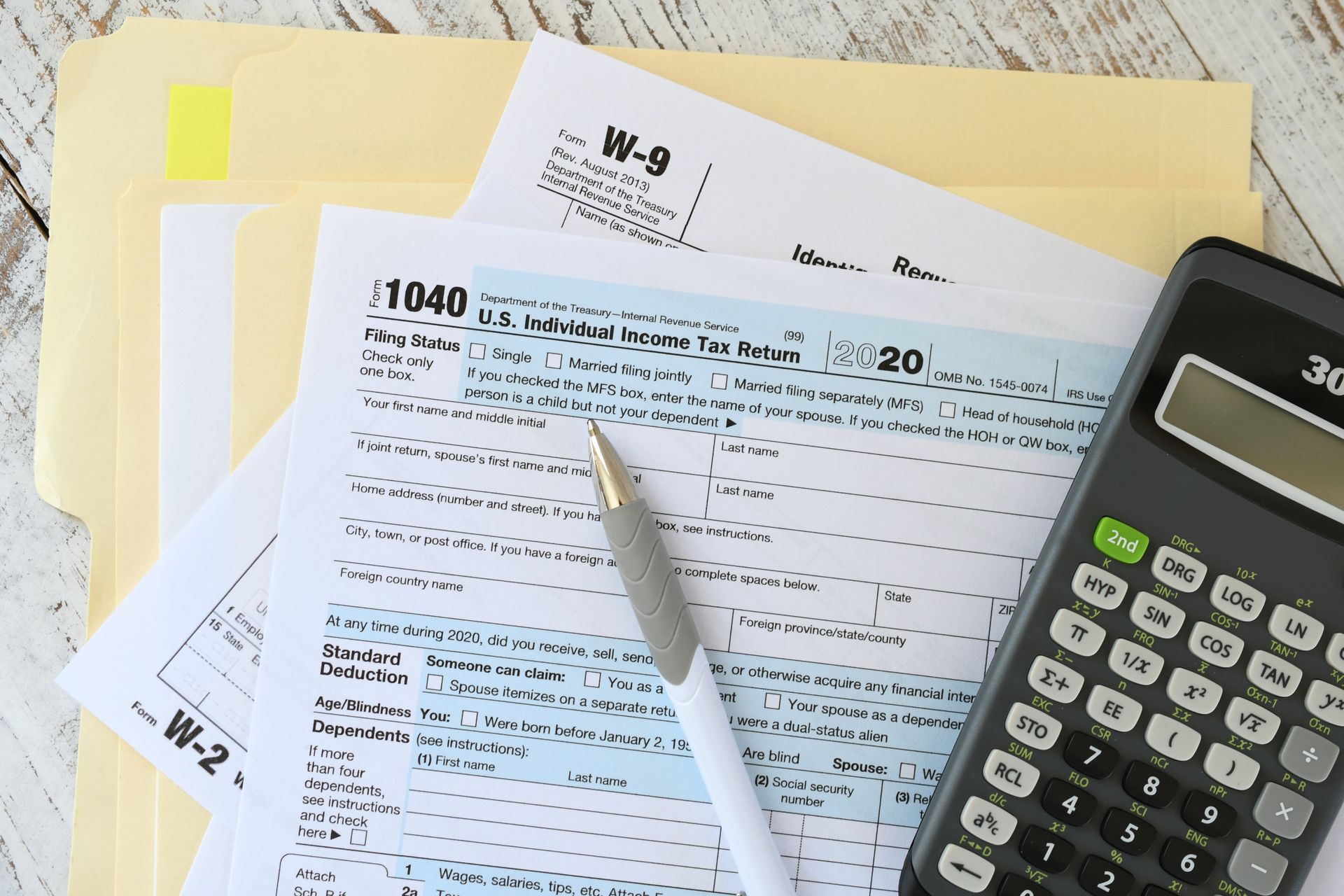Tax forms, pen, and calculator on a desk.
