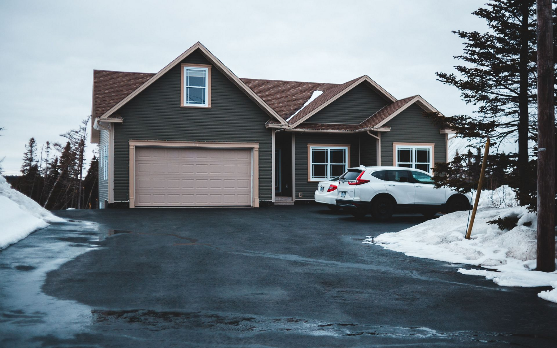 Snowy suburban house with a garage and a white car parked in the driveway