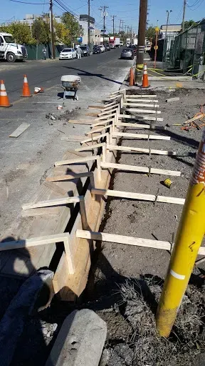 Construction of a concrete curb on a city street. Wooden forms and orange cones are present.