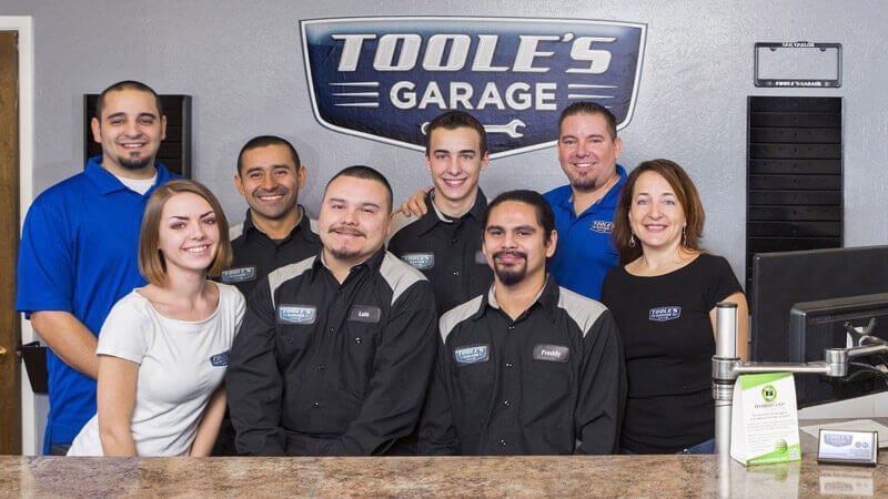 A group of people are posing for a picture in front of a toole 's garage sign.