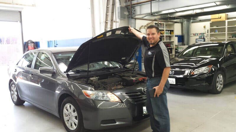 A man is standing in front of a car with the hood open