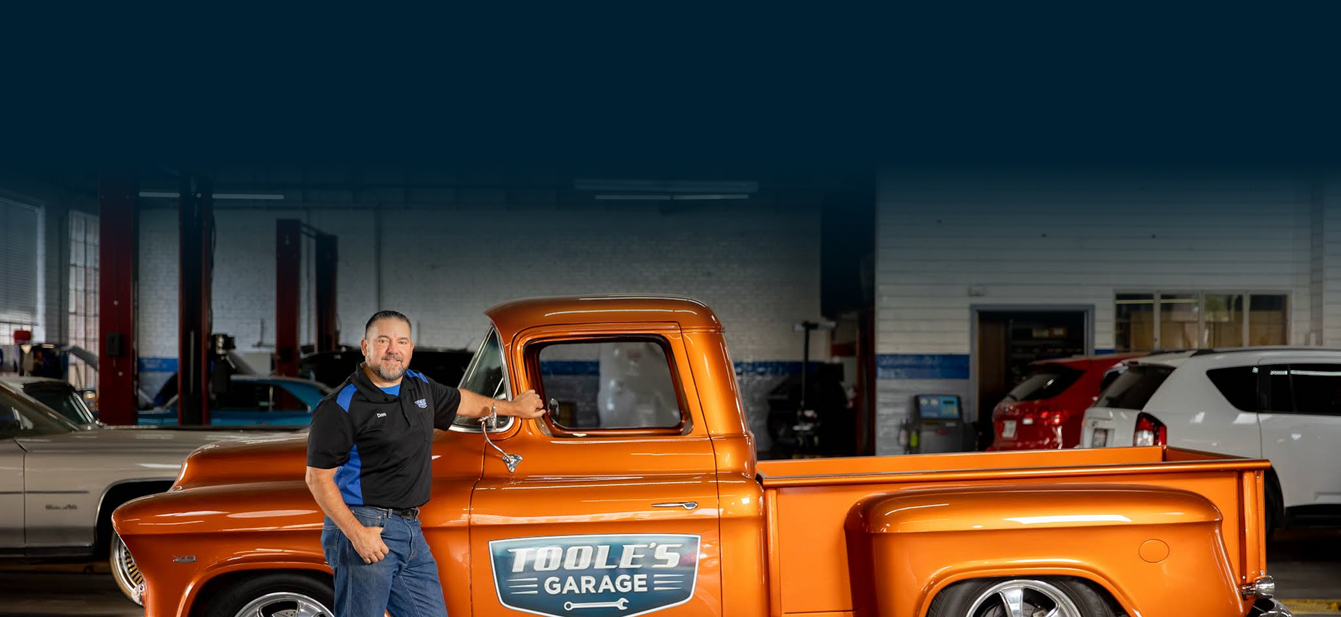 A man is standing next to an orange truck in a garage.