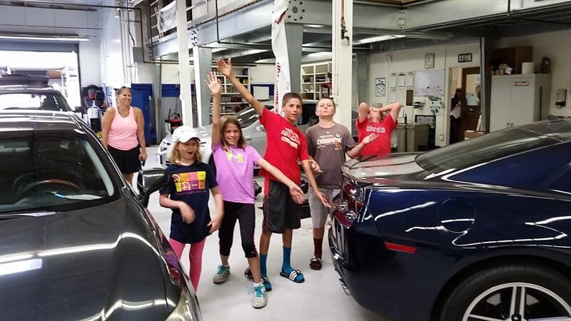 A group of people standing in front of cars in a garage