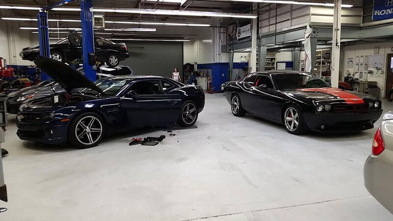 Two cars are parked in a garage with their hoods open.