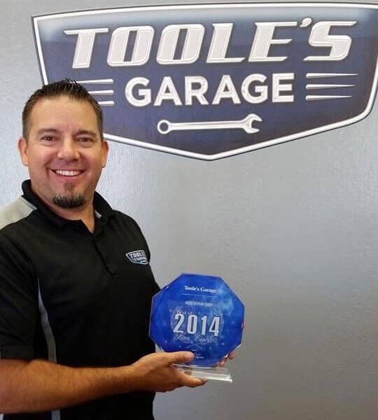 A man holding a trophy in front of a sign that says tools garage
