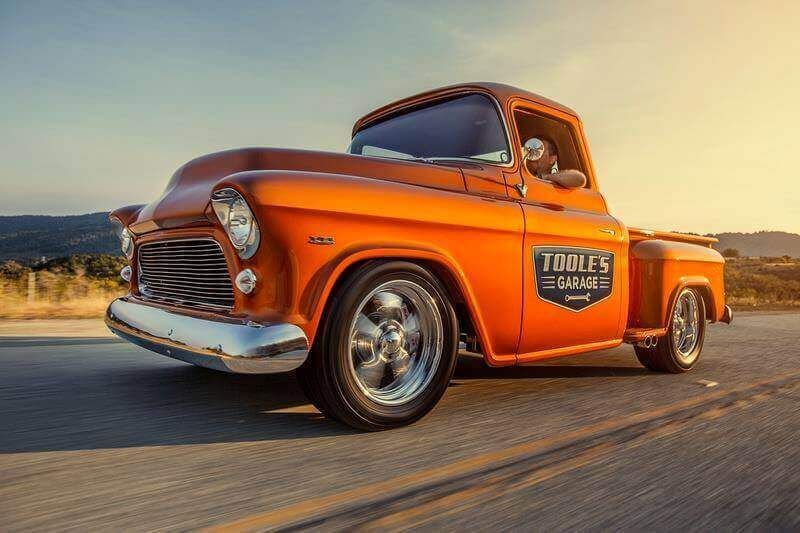 An old orange truck is driving down a road.