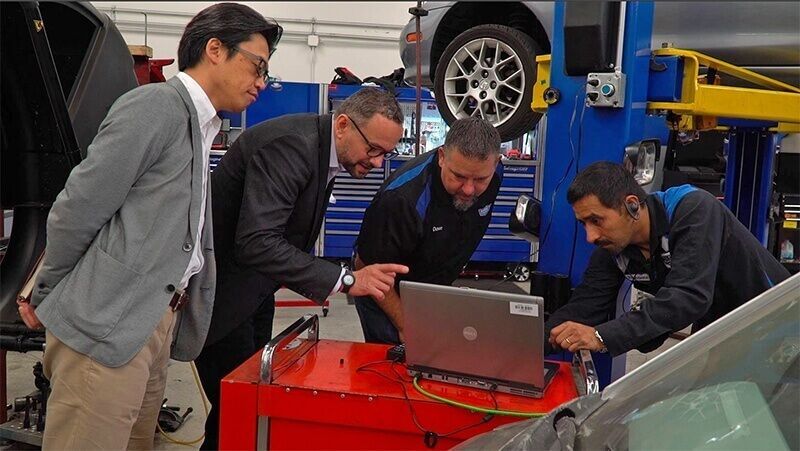 A group of men are looking at a laptop in a garage.