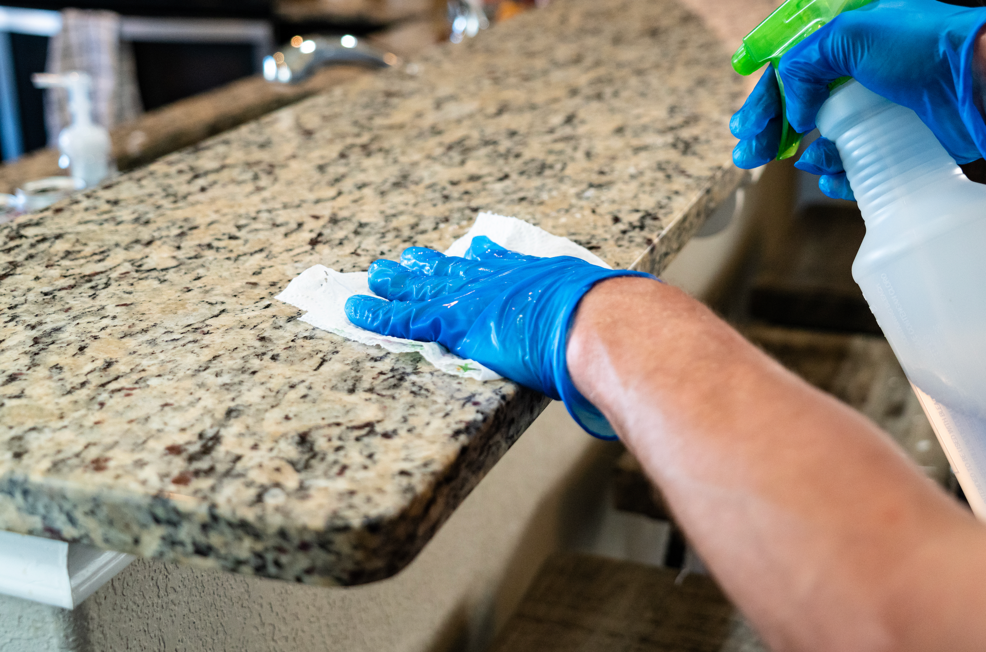 A person is cleaning a granite counter top with a spray bottle and a cloth.