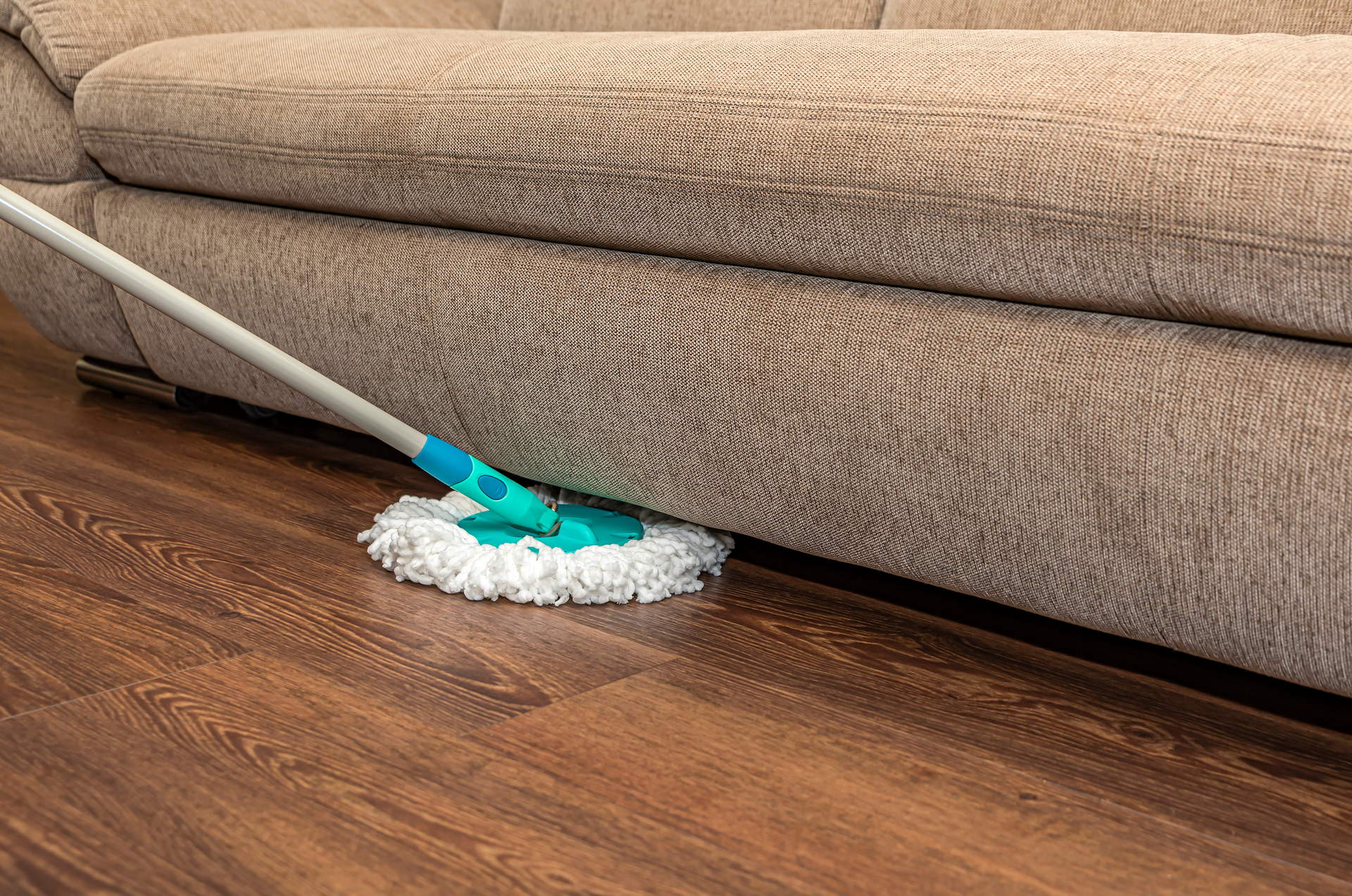 A mop is being used to clean a couch in a living room.