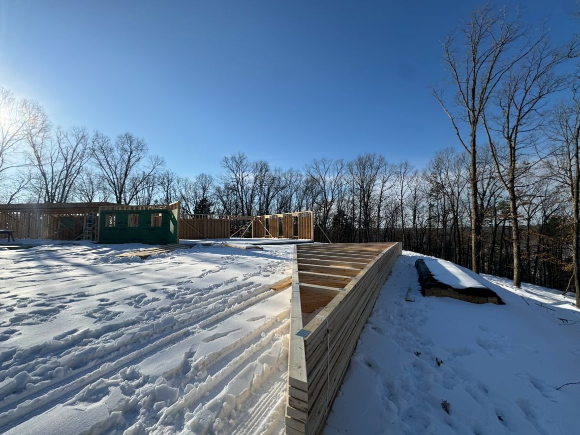 Snow-covered rooftop with wooden ledge beside a wooded yard under a clear blue sky