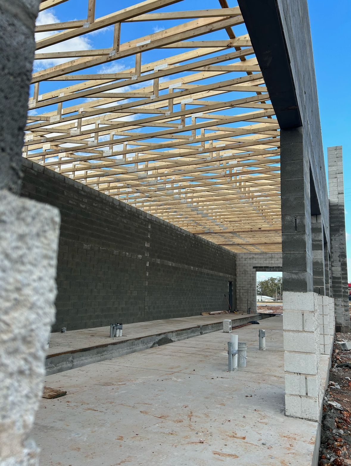 Unfinished concrete building interior with exposed wooden roof trusses and open walls.
