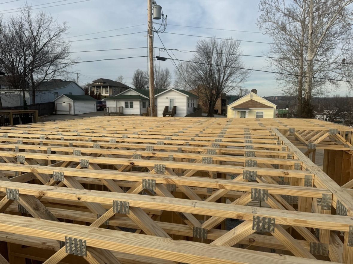 A construction site featuring an unfinished wooden floor joist system for a building frame against a suburban backdrop.