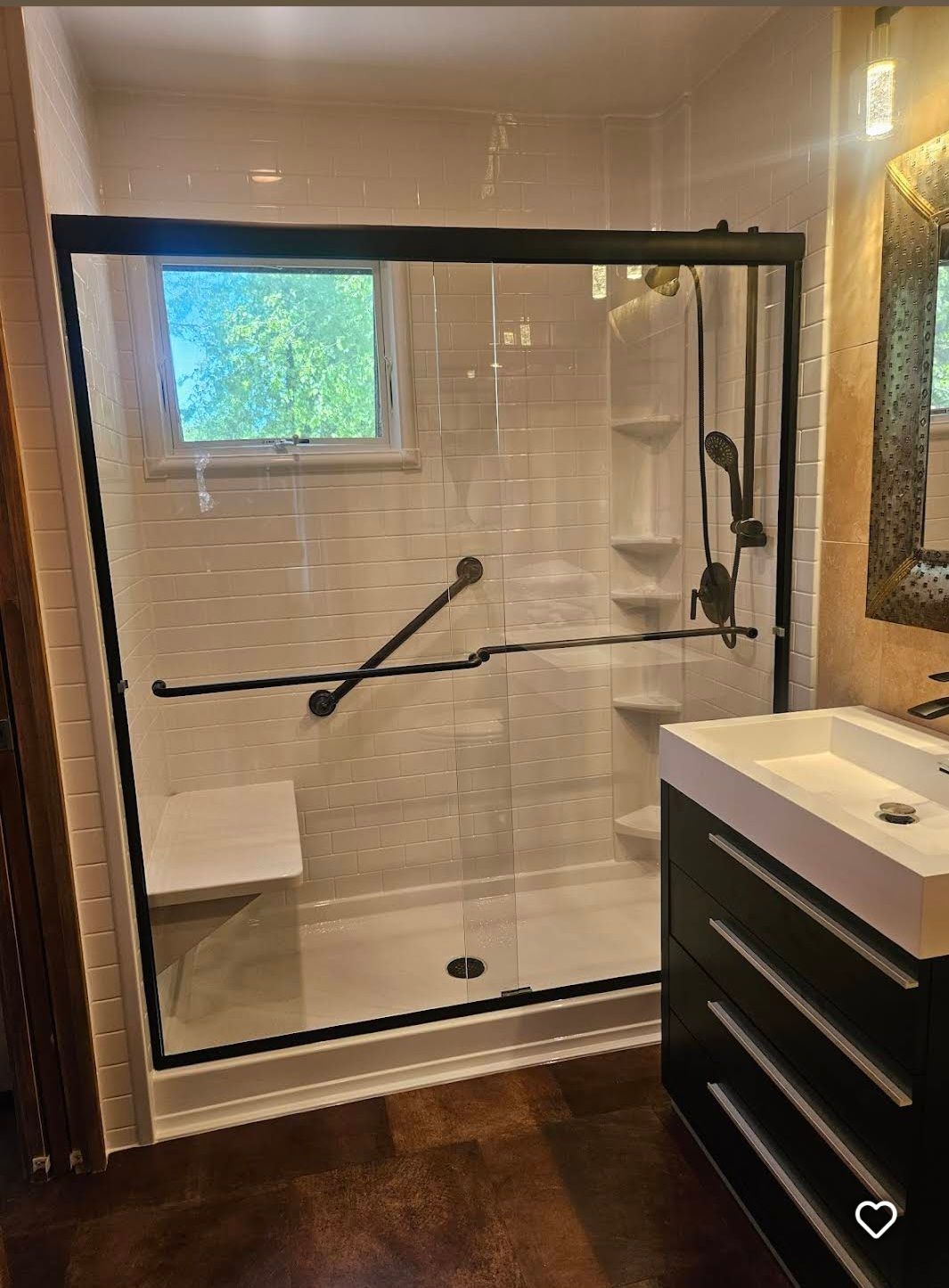 A modern walk-in shower with dark, textured stone walls, a rainfall showerhead, a handheld sprayer, and wood bench seating.