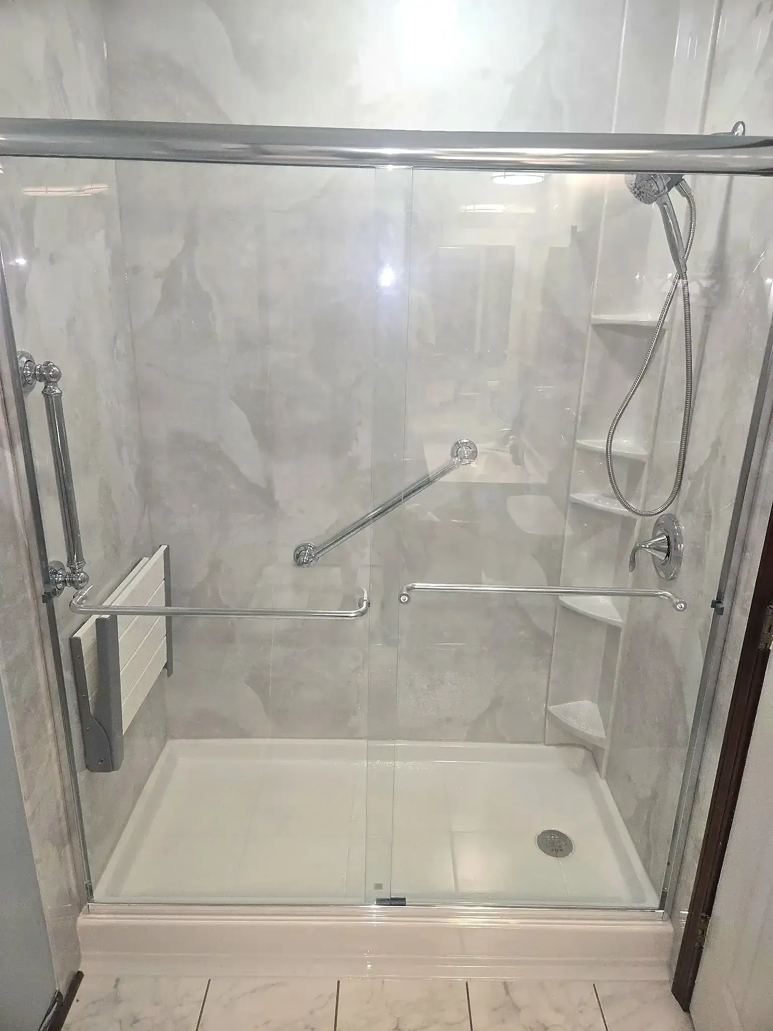Accessible shower stall with grab bars, shelves, and sliding glass doors.