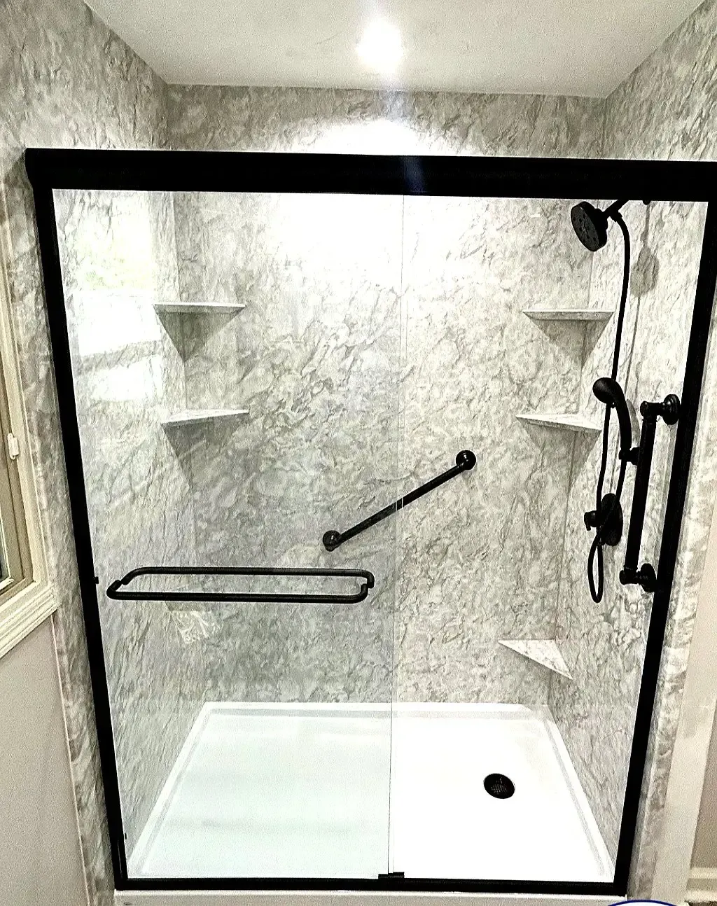 Black-framed shower stall with gray walls, built-in shelves, grab bar, and black shower fixtures.