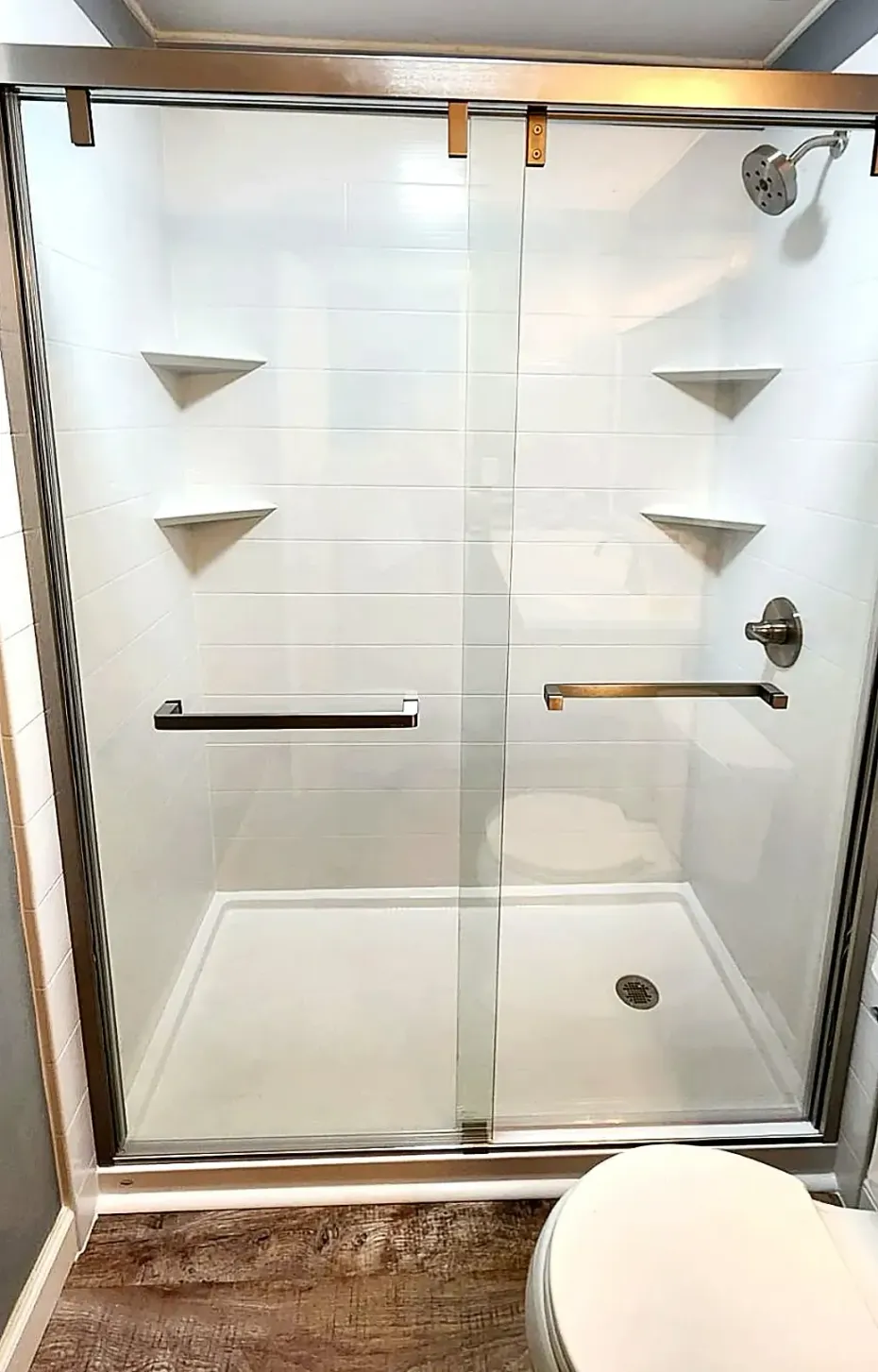 A white walk-in shower stall with glass sliding doors, built-in corner shelves, and a chrome shower head and handle.