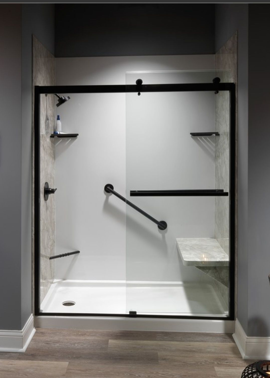 Modern walk-in shower with white walls, black hardware, glass sliding doors, grab bars, corner shelves, and a built-in seat.