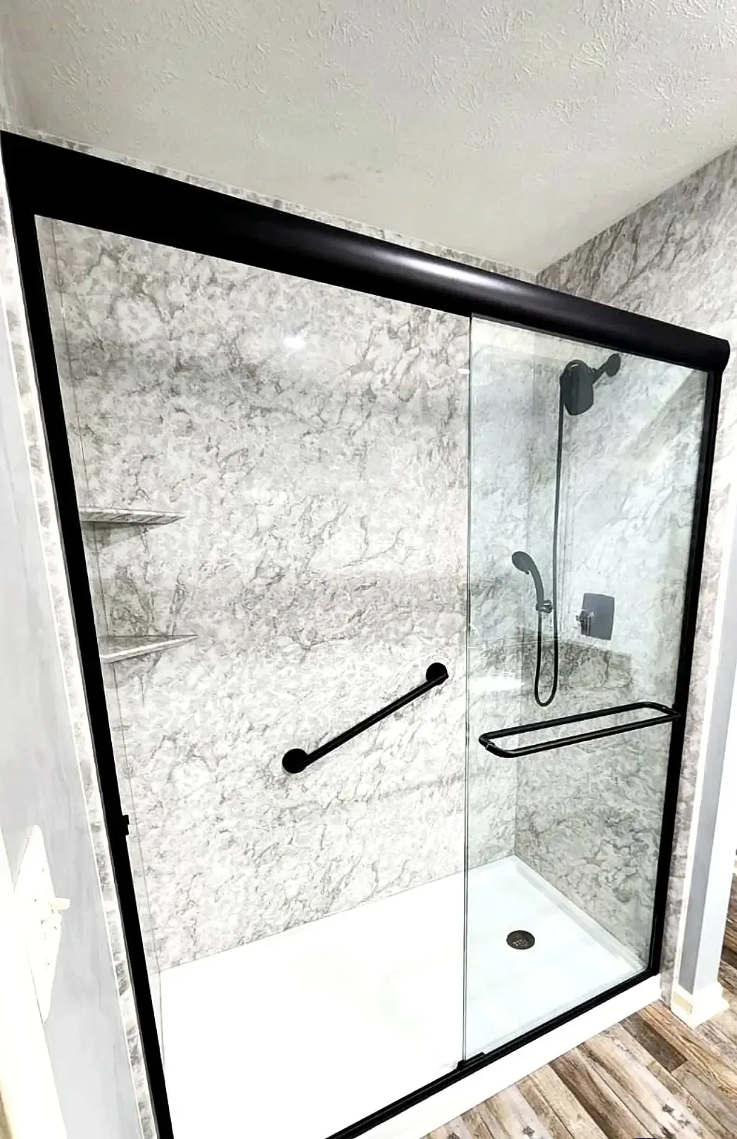 A modern shower stall with black trim, a sliding glass door, grab bars, and a shower head.
