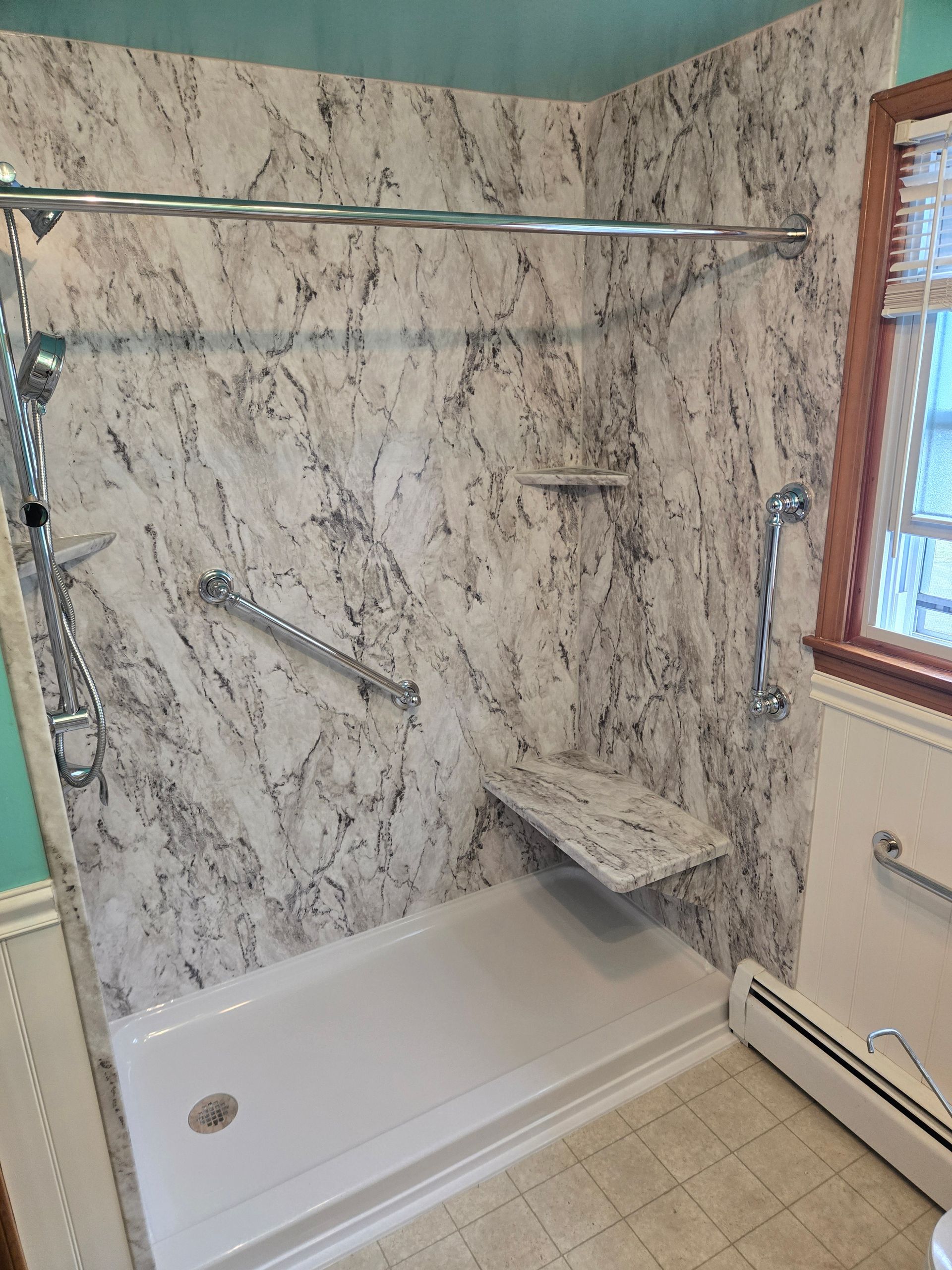 Accessible shower stall with white and gray marble-patterned walls, grab bars, a built-in seat, and a low-profile base.