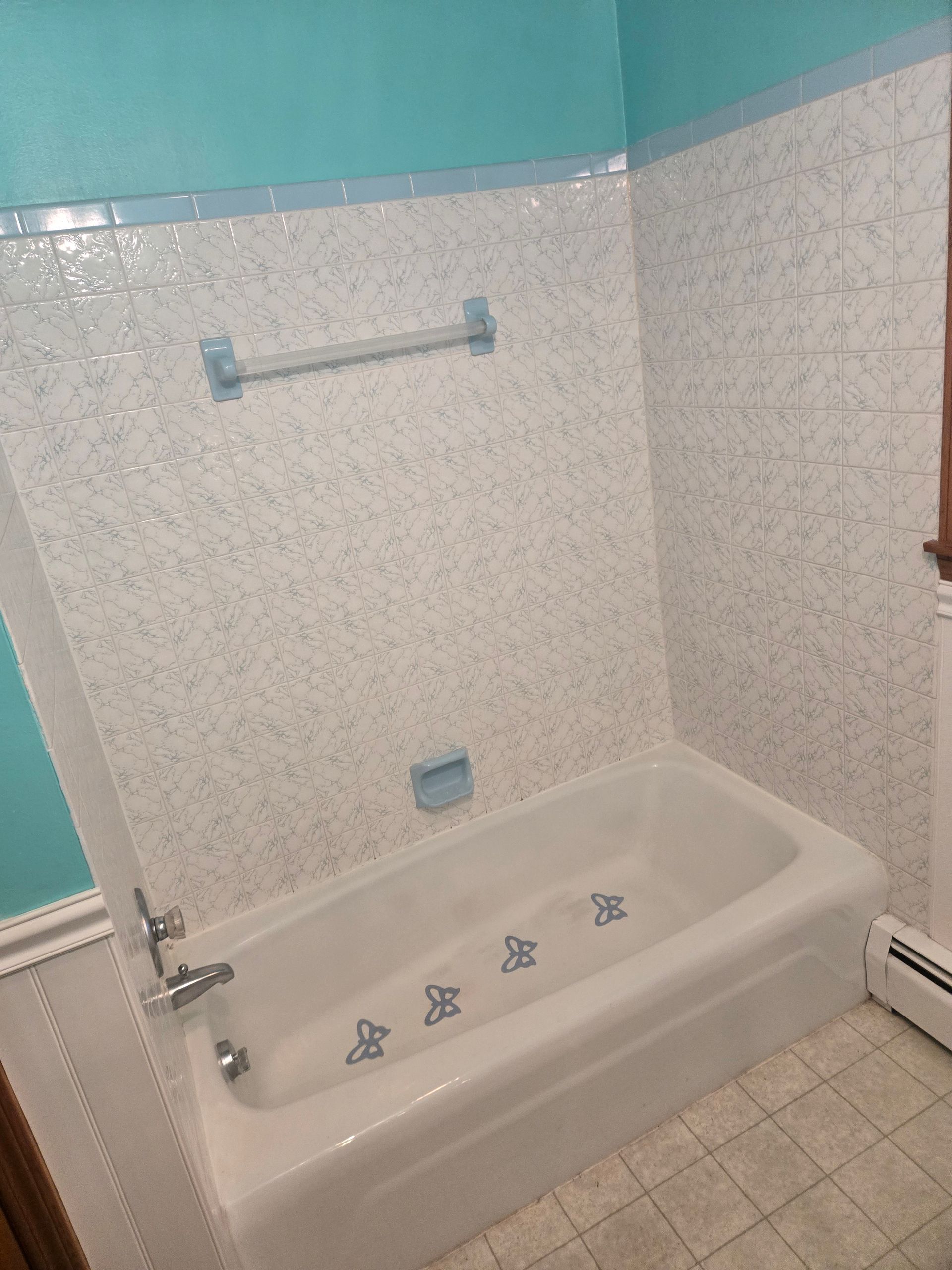 A white bathtub with blue butterfly decals, surrounded by speckled white tile walls and bright teal-painted upper walls.