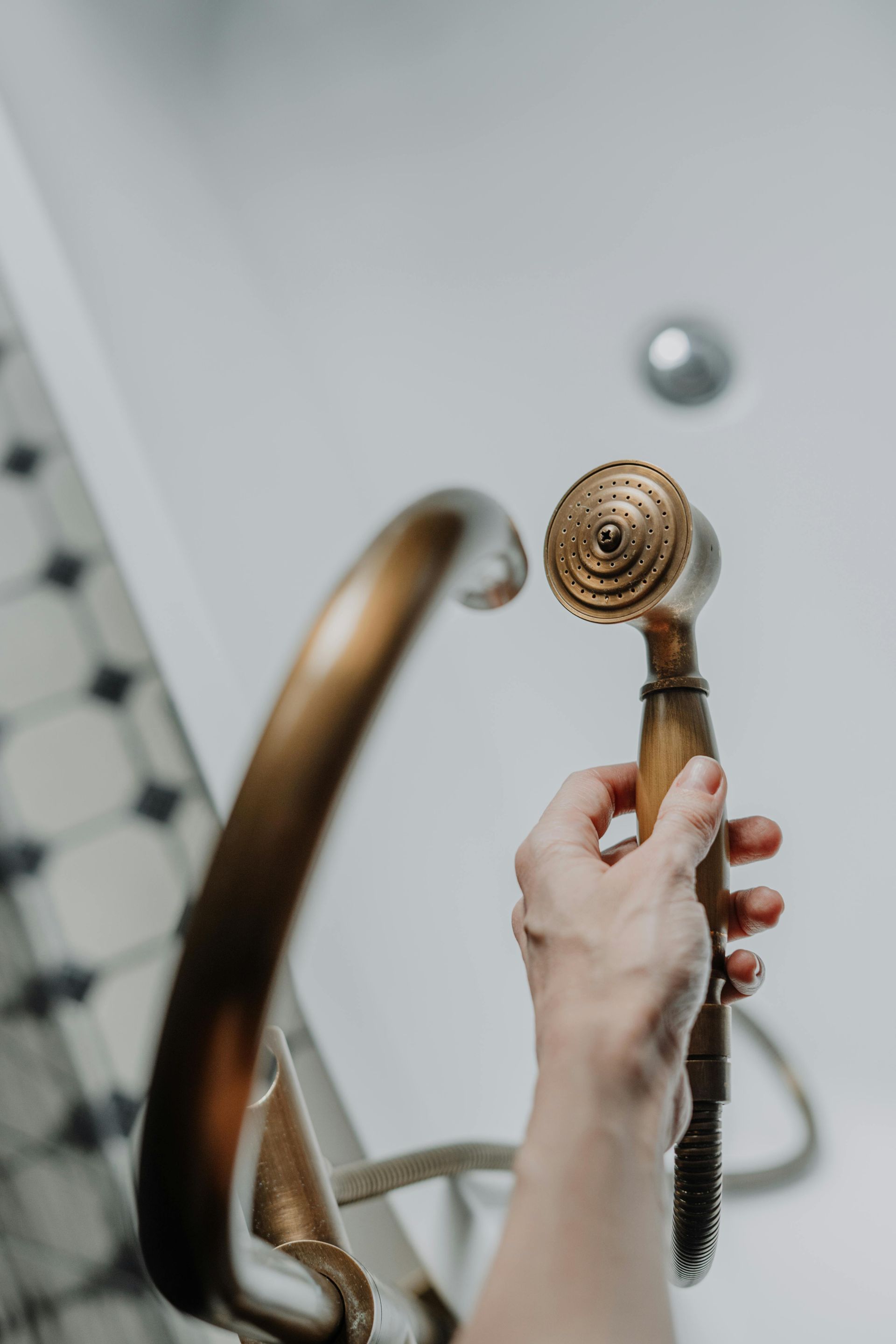Hand holding a bronze handheld showerhead in a tiled bathroom