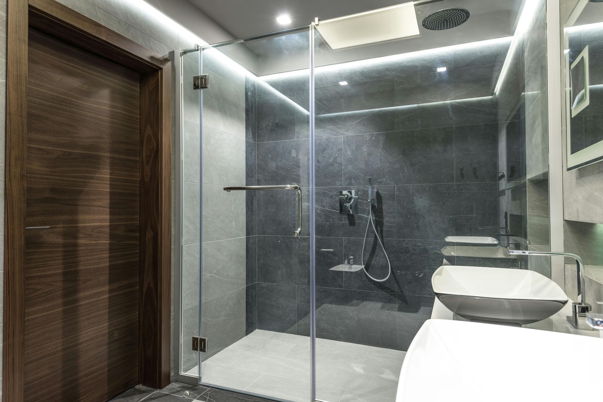 Modern bathroom with glass shower, dark tile walls, and a wall-mounted sink