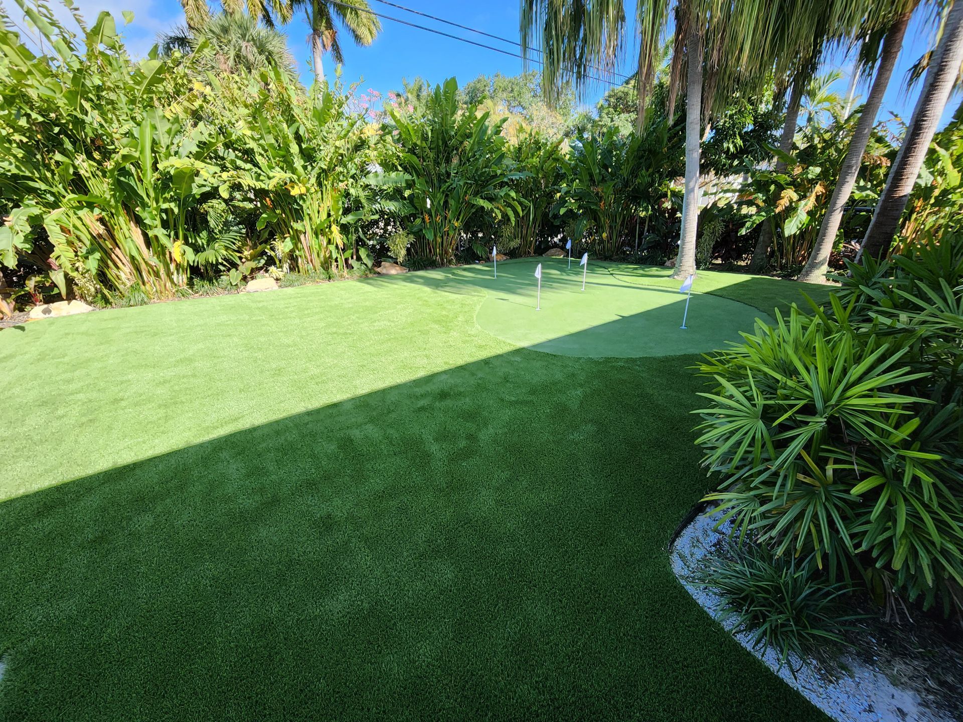 There is a putting green in the middle of a lush green field surrounded by palm trees.