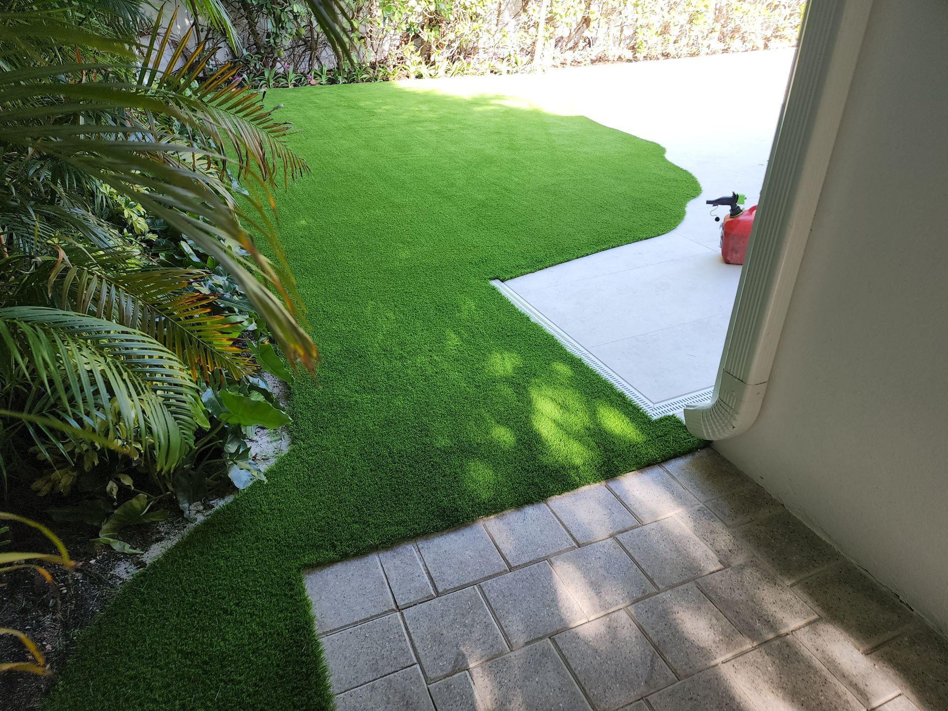 A lush green lawn is surrounded by palm trees and a brick walkway.