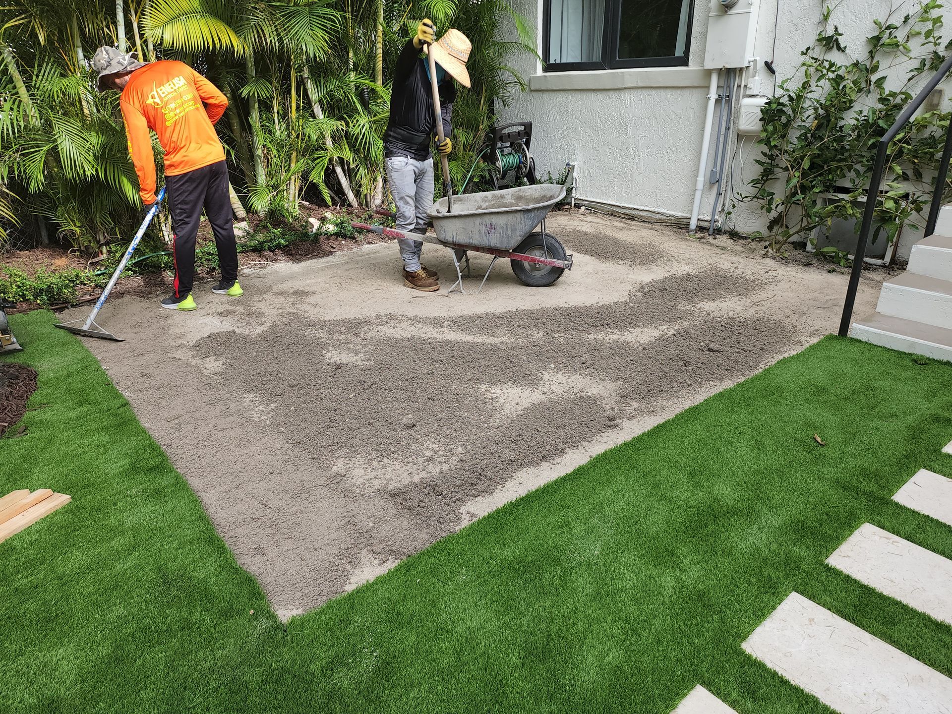 Two men are working on a patio in a backyard.