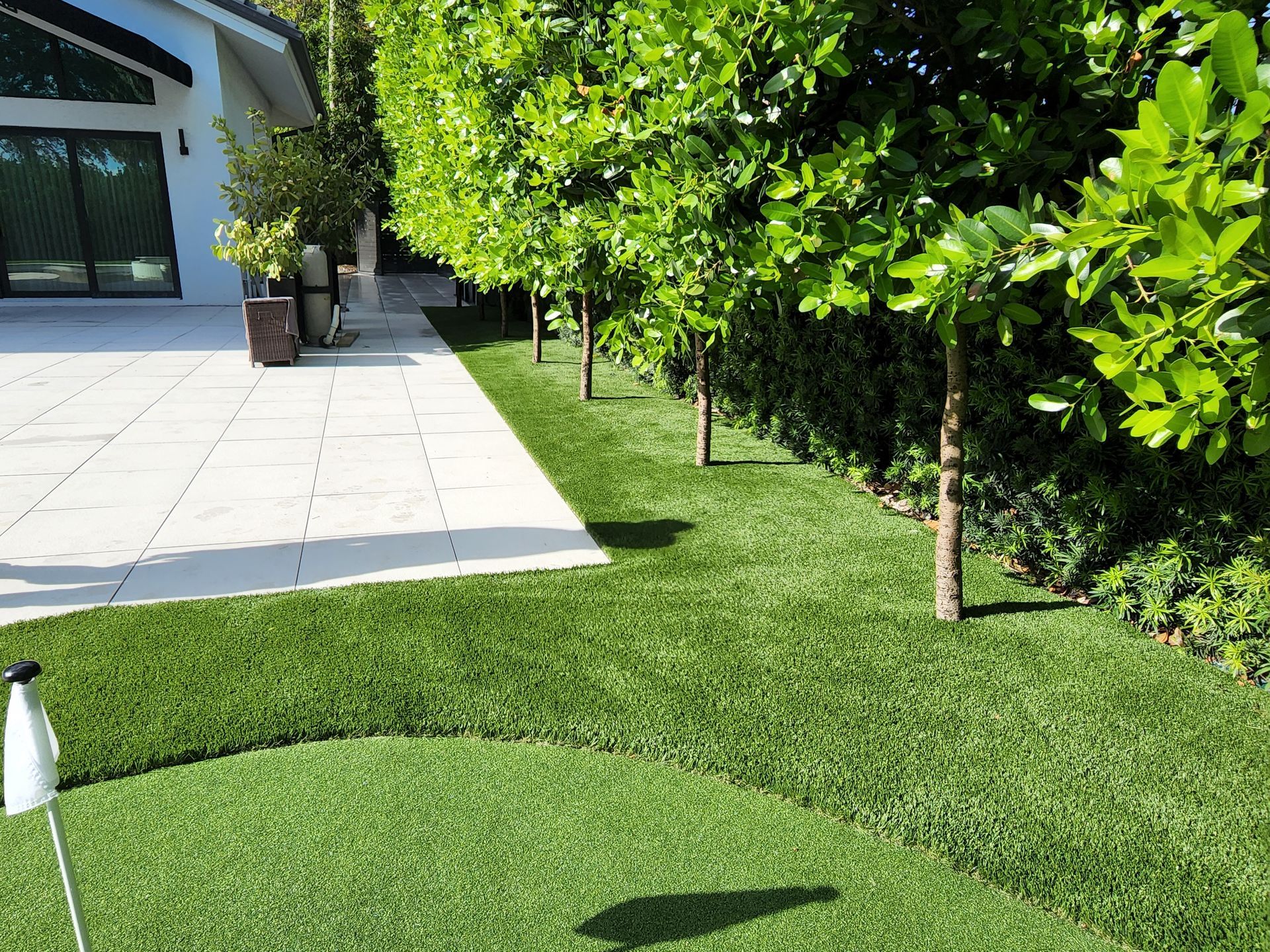 A lush green lawn with trees and a white house in the background.