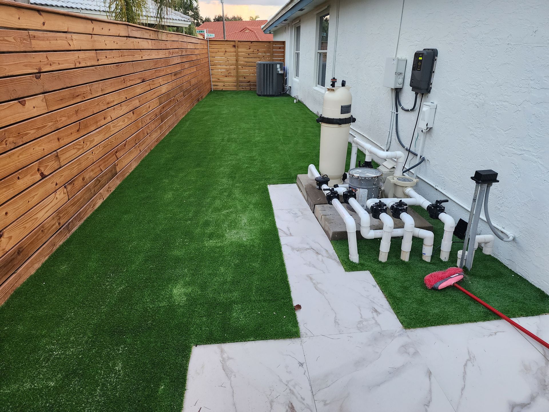 A backyard with a fence , grass , pipes and a pool filter.